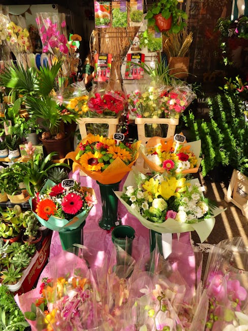 A display of fresh floral arrangements at a florist shop, featuring a variety of vibrant bouquets with roses, gerbera daisies, and chrysanthemums in shades of yellow, pink, red, and white. The flowers